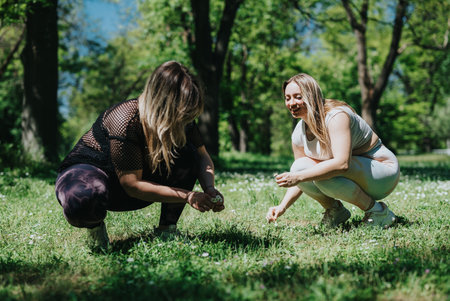 Two female friends enjoying nature, gathering flowers on a sunny day in a lush green parkの写真素材