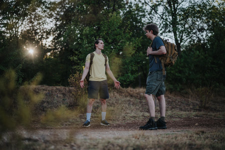 Two hikers with backpacks talk on a forest trail at sunset, capturing outdoor adventure and...