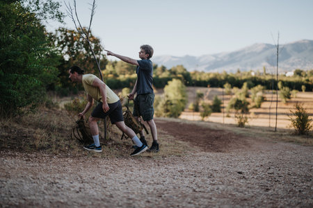 Two friends hike together with backpacks in a rural landscape with mountains in the distanceの写真素材