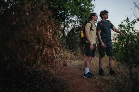 Two hikers with backpacks standing on a dirt trail, discussing their route in a forest