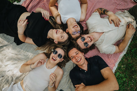 Group of friends enjoying a picnic in the park, smiling and laying togetherの写真素材