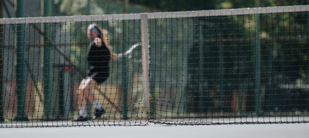 Tennis player in action on an outdoor court behind the net during practiceの写真素材