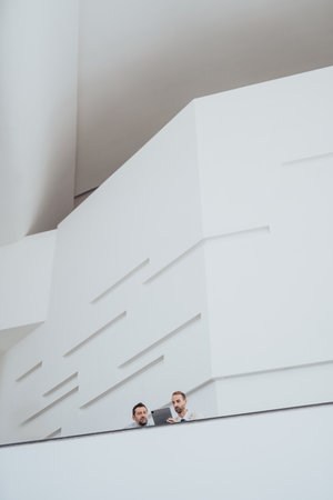 Executives and colleagues review ideas on a clean white modern balcony, engaged in discussionの写真素材