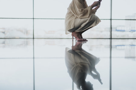 Crouching professional in beige outfit with pink heels, reflected on a glossy floor in a modern settingの写真素材