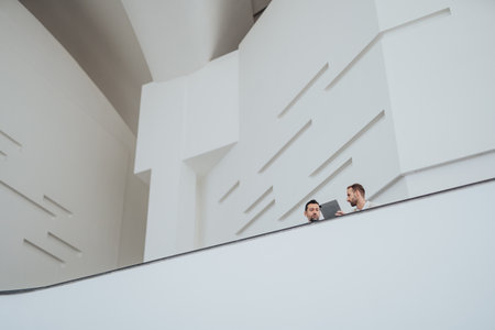 Two colleagues on a modern white balcony working with a tablet in a minimal spaceの写真素材