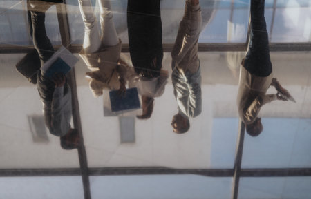 People standing and discussing documents reflected in a glass floor inside a modern office environmentの写真素材