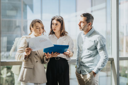 Three colleagues review documents in a bright modern office during a collaborative discussionの写真素材