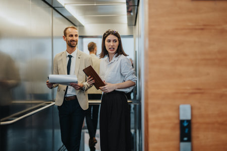 Business colleagues in a modern office discuss documents in a crowded elevator lobbyの写真素材