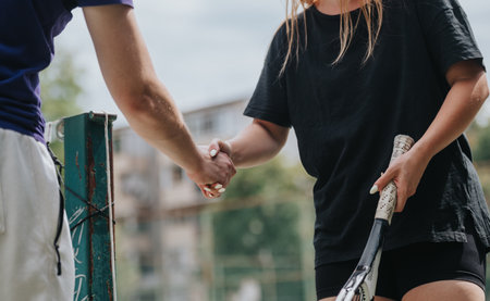Two people shake hands after an outdoor tennis session, signaling teamwork and friendship.の写真素材