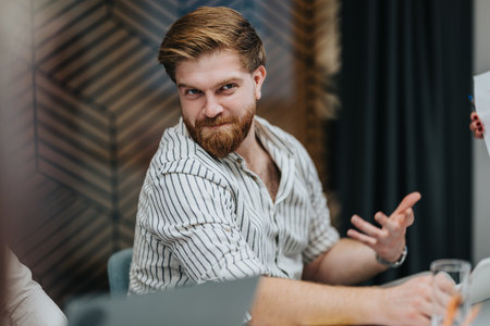 Confident man with striped shirt gestures during a business meeting in a modern officeの写真素材