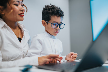 Two people study together at a laptop in a modern classroom with focused expressionsの写真素材
