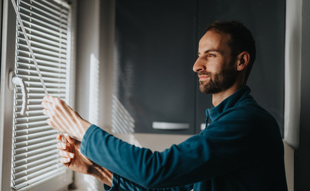 Man adjusting blinds in a bright modern interior space at homeの写真素材