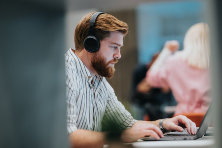 Man with headphones typing on laptop in an office, focused workspace scene