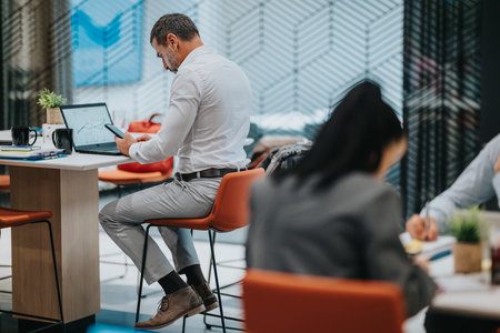 Business professional at a modern office desk using a laptop and phone during a busy workdayの写真素材