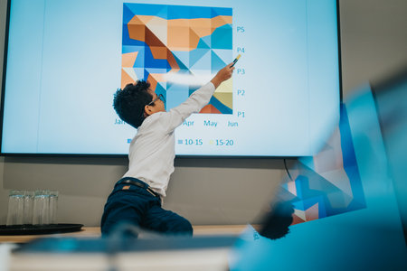 Young presenter points to a colorful geometric chart during a business presentation in a modern officeの写真素材