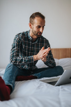 Man having a video chat while seated comfortably on his bedの写真素材