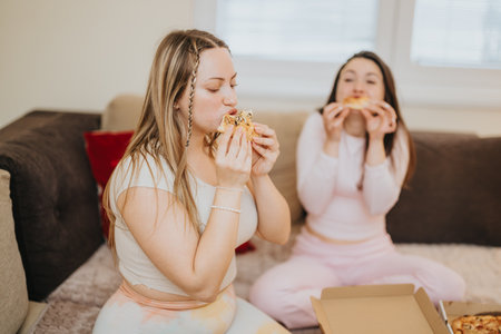 Friends enjoying slices of pizza while relaxing in a cozy living roomの写真素材