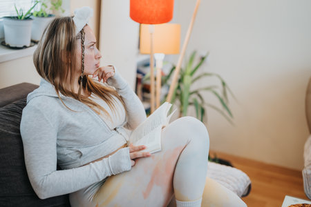 Woman reading a book at home while sitting comfortably on the couchの写真素材