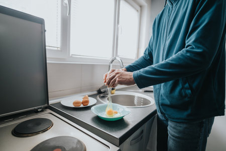 Man breaking eggs in kitchen preparing for cookingの写真素材