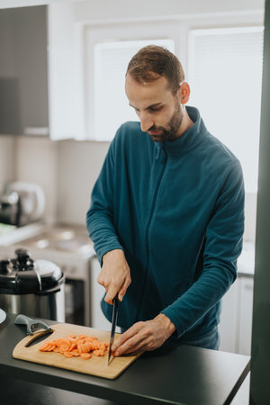 Man chopping fresh carrots on a cutting board in a modern kitchen.の写真素材