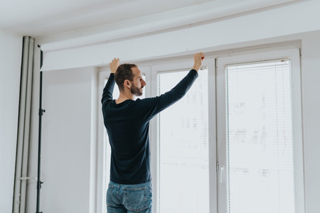Man adjusting window blinds in a bright and minimalist roomの写真素材