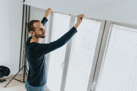 Man adjusting blinds near a large window in a modern homeの写真素材