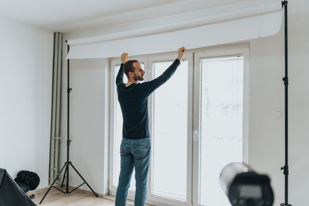 Man adjusting a studio setup with photography equipment in a home settingの写真素材