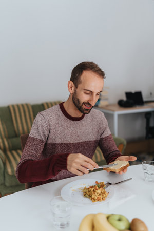 Man enjoying a meal while spreading butter at homeの写真素材