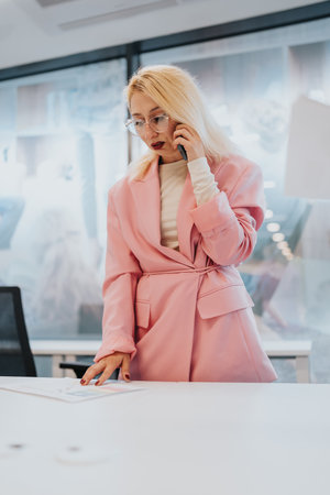Businesswoman in pink blazer makes a phone call in a modern, bright office settingの写真素材