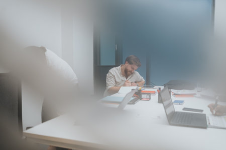 Focused man writes at a bright office desk during a collaborative team session