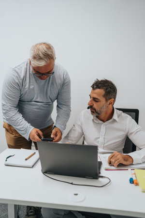 Collaborating colleagues review data on laptop in a modern office during a business meetingの写真素材