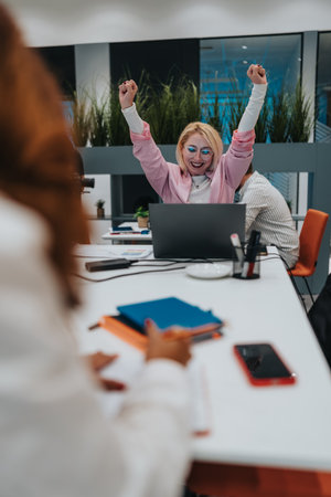 Celebrating teamwork: a motivated office team cheers beside a laptop during a busy meeting