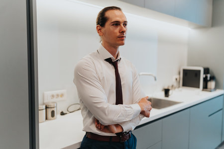 Professional man in a modern office kitchen standing with arms crossed, business portraitの写真素材