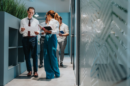 Team of professionals reviewing documents in a modern office hallway during a collaborative work sessionの写真素材