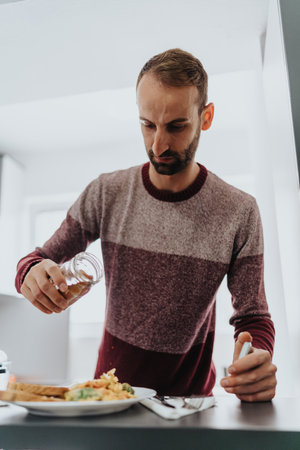 Man in a sweater seasoning food in a modern kitchenの写真素材