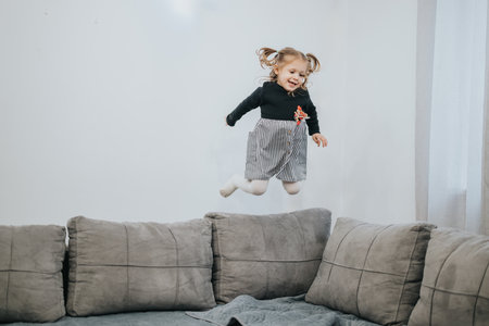Happy child joyfully jumping on a comfy couch in a bright living roomの写真素材