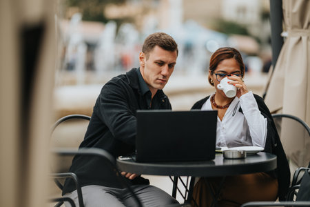 Two people at an outdoor cafe work on a laptop, sharing coffee and ideas in a casual meetingの写真素材