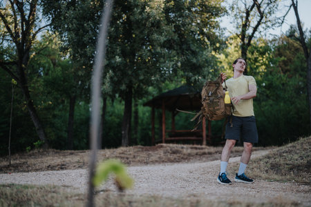 Hiker with large backpack stands on a dirt path in a park, looking up, ready for outdoor adventure