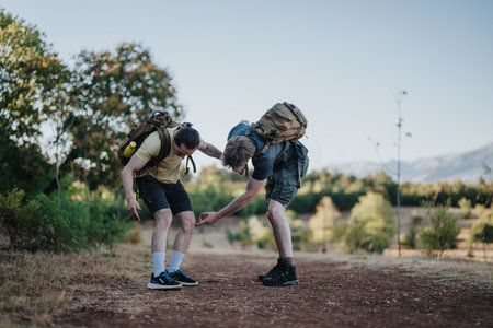 Two hikers lend a helping hand on a dirt trail during an outdoor adventureの写真素材