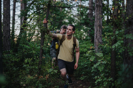 Two hikers navigate a forest trail, supporting each other on a rugged woodland hike today
