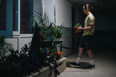 Man tending to potted plants in a dim indoor corridor with greeneryの写真素材