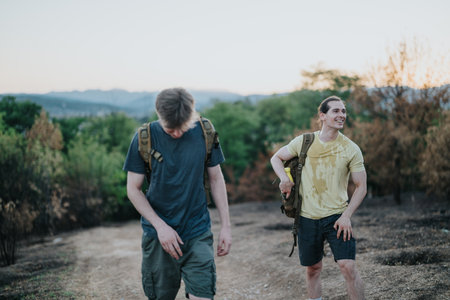 Two friends hiking on a sunlit trail with backpacks in a scenic outdoor settingの写真素材