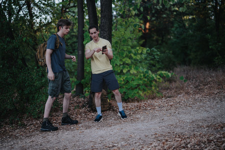 Two friends hike in the forest, checking a phone together during an outdoor adventureの写真素材