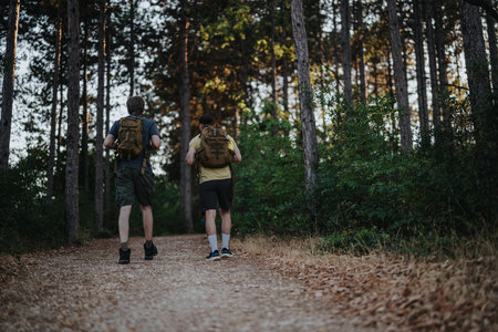 Two hikers walk along a forest trail with backpacks, enjoying an outdoor adventure togetherの写真素材