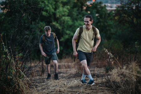Two hikers hiking up a trail with backpacks through a dry grass and forest landscape.
