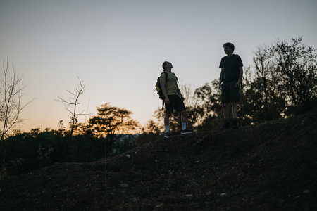 Two hikers stand on a hill at sunset, sharing a quiet moment during an outdoor hikeの写真素材