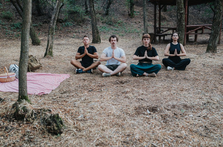 Four friends meditate in a forest clearing with a picnic blanket during an outdoor gatheringの写真素材