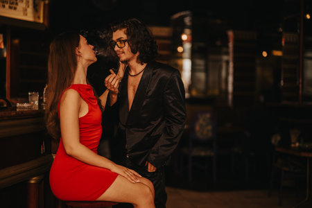 Romantic night out at a dimly lit bar with a couple in stylish outfits sharing a quiet momentの写真素材