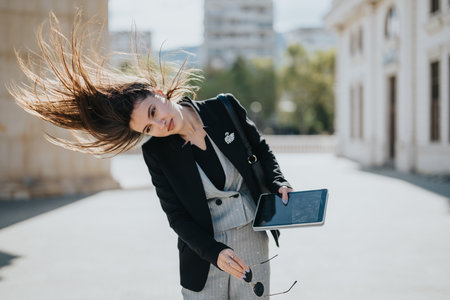 Businesswoman outdoors with tablet and sunglasses, wind in her hair, stylish urban portraitの写真素材