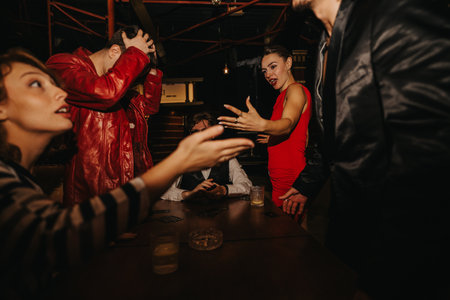 Friends enjoy a lively night out at a stylish bar, featuring a woman in a red dress speaking animatedly to the groupの写真素材